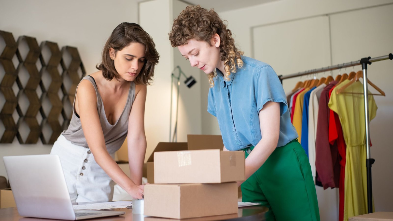 Dos emprendedoras preparan cajas para enviar pedidos junto a una notebook