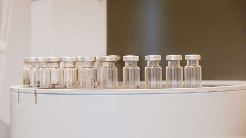 Fila de frascos de vidrio transparentes con tapa metálica sobre un equipo de laboratorio
