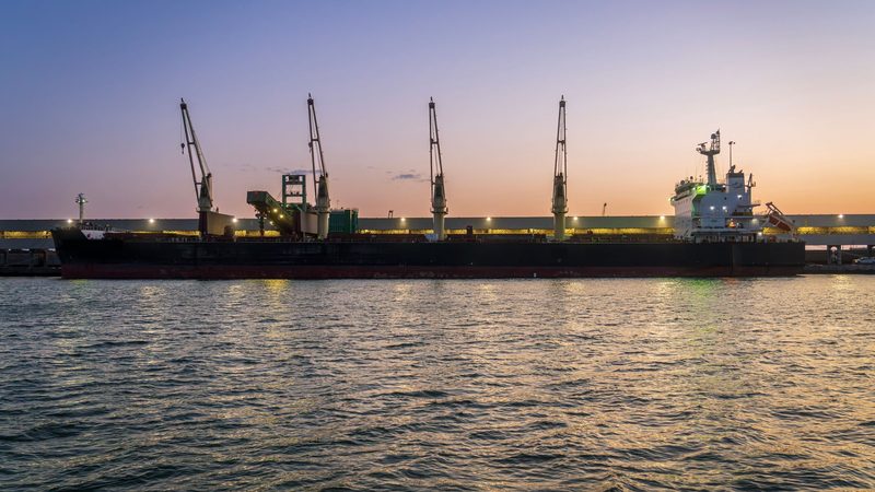 Buque granelero amarrado en un puerto al atardecer, con sus grúas de carga