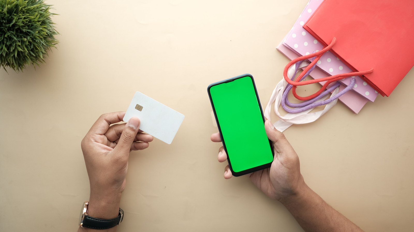 Manos sosteniendo un celular y una tarjeta, junto a bolsas de compras, en una escena de compra online