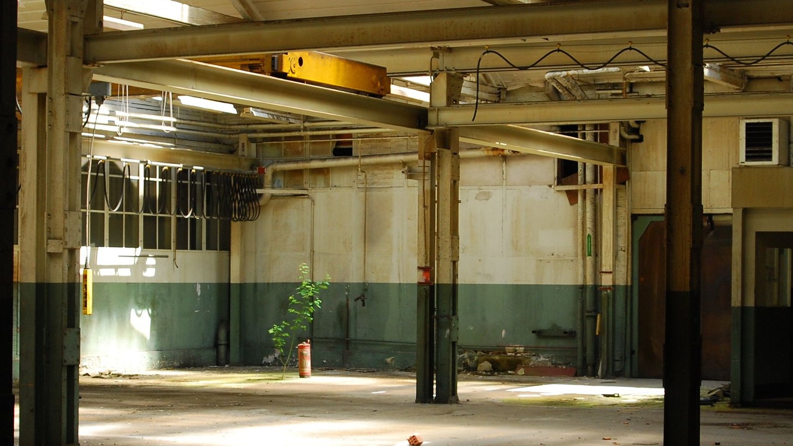 Interior de una nave industrial vacía, con columnas de acero y grúa puente