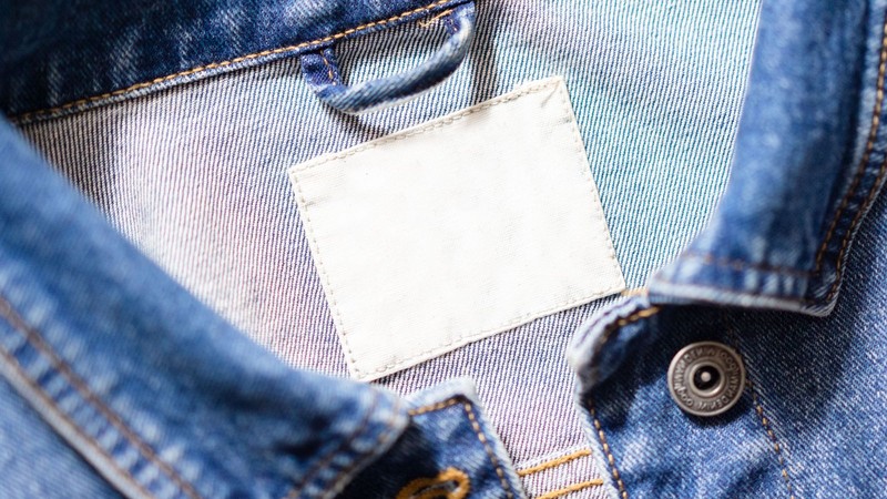 Etiqueta de tela en blanco cosida en el cuello de una prenda de jean