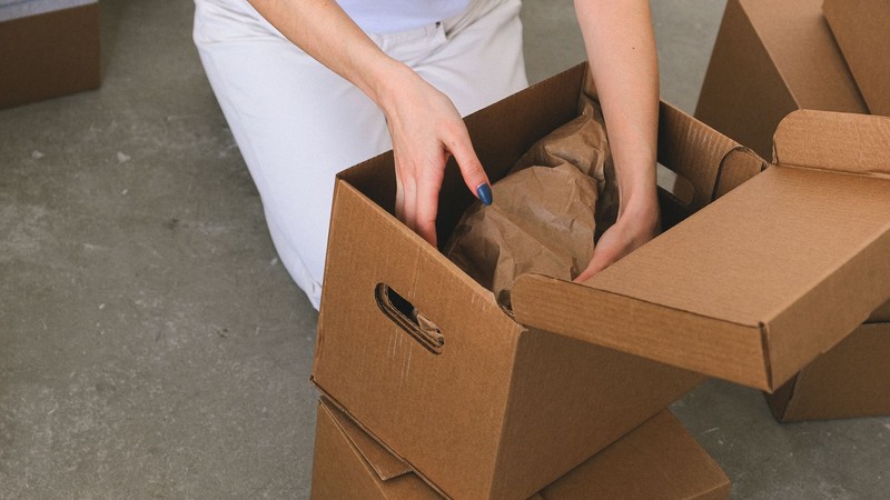 Manos de una persona empaquetando objetos en una caja de cartón con papel de embalaje