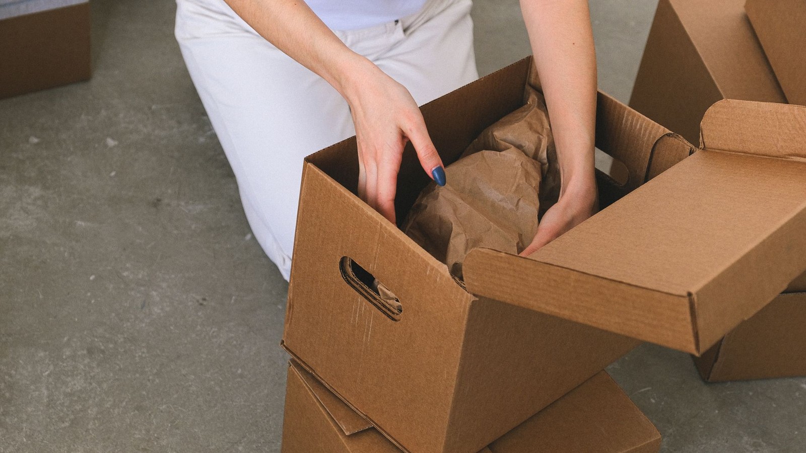 Manos de una persona empaquetando objetos en una caja de cartón con papel de embalaje