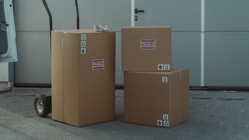 Cajas de cartón embaladas para envío, apiladas junto a un carrito de carga, de cerca
