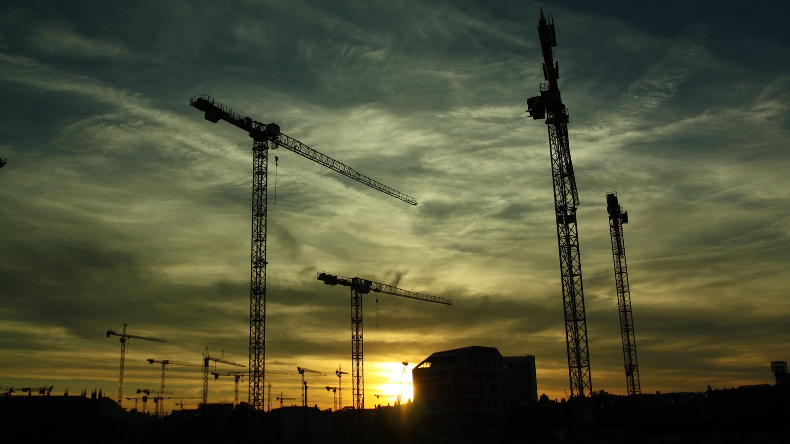 Siluetas de varias grúas de construcción a contraluz contra un atardecer