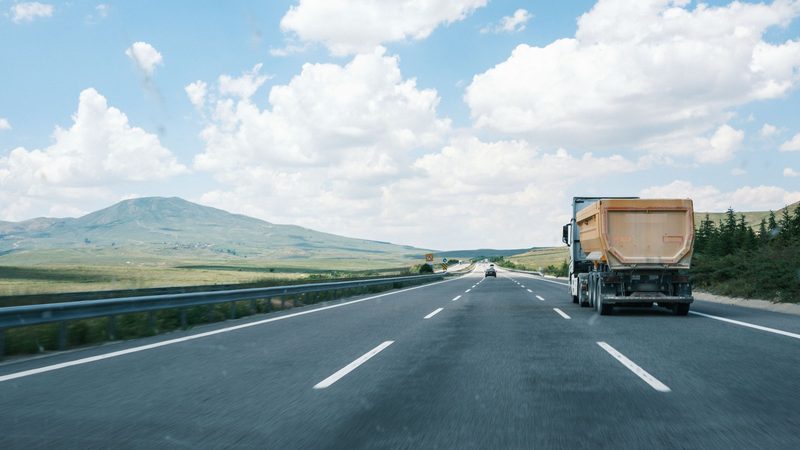 Camión de carga en una autopista entre campos y sierras, bajo un cielo con nubes