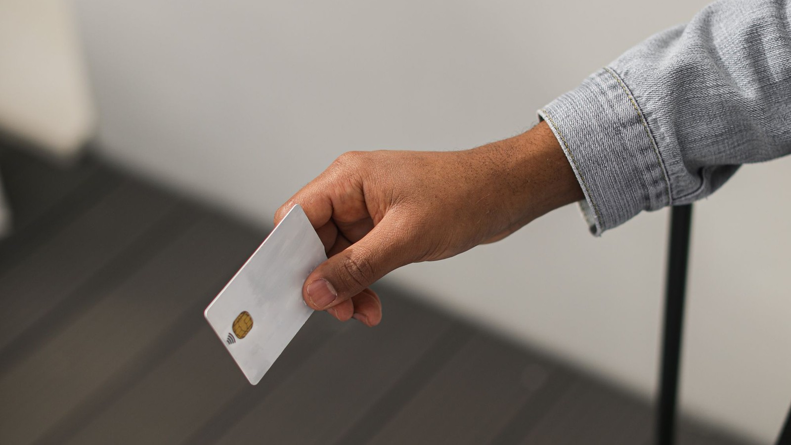 Mano sosteniendo una tarjeta con chip, brazo extendido sobre un fondo neutro