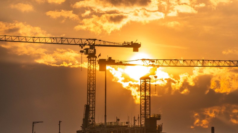 Dos grúas torre recortadas contra un atardecer anaranjado sobre una obra en construcción